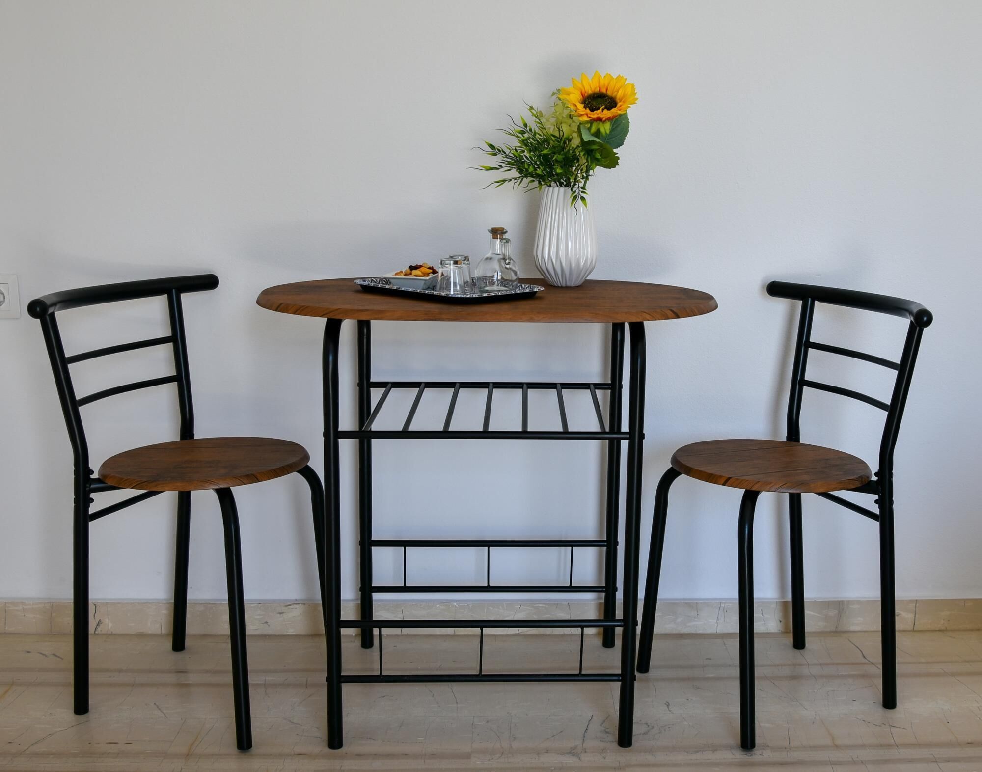 A small round table with two chairs, a vase with flowers, and a tray with snacks.