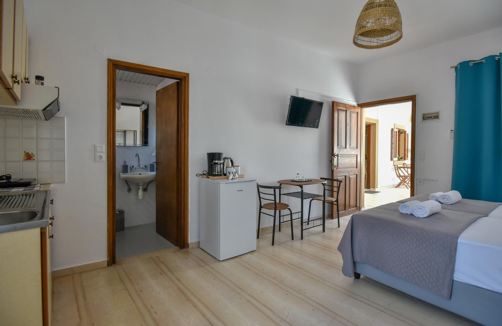 A compact hotel room with a bed, a small kitchenette, a sink, a dining area, and a TV.