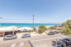 A coastal road with parked cars, a beachside café, and a clear view of the ocean.