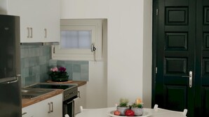 A modern kitchen with white cabinets, a black refrigerator, and a dining area with a white table and chairs. - Lenko Bianco Studio by Estia (Corfu)
