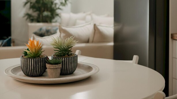A kitchen with a white table, three striped pots with plants, a refrigerator, and a window. - Lenko Bianco Studio by Estia (Corfu)