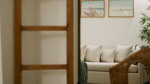 An open wooden door leading to a living room with a sofa, two framed pictures on the wall, and a potted plant. - Lenko Bianco Studio by Estia (Corfu)