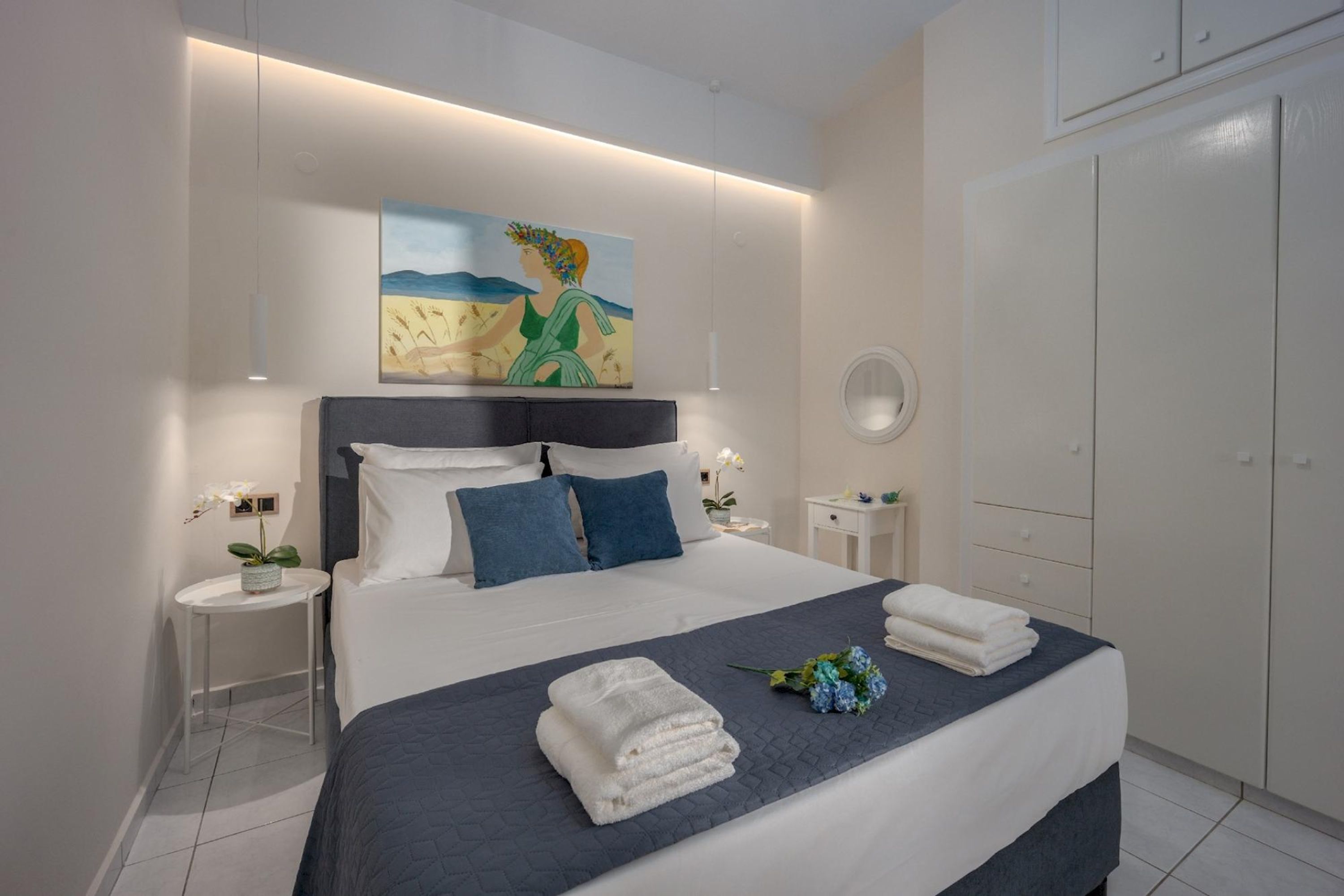 Un dormitorio moderno con una cama grande, paredes blancas, un cuadro sobre la cama y un armario a la derecha.