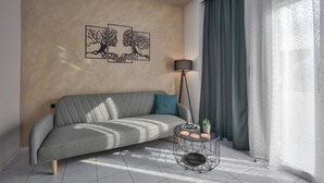 Una sala de estar moderna con un sofá gris, una mesa redonda de centro y una lámpara de pie. Hay dos obras de arte en la pared sobre el sofá.