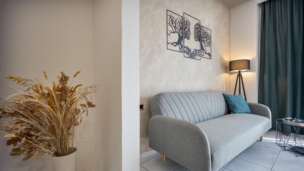 Un soggiorno moderno con un divano grigio, una lampada da terra e un vaso con piante essiccate.