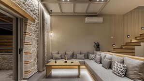 Un salon moderne avec un mur en pierre, un banc en bois, un canapé gris agrémenté de coussins à motifs et un escalier.