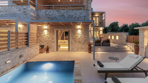 Une maison en pierre à deux étages, dotée d’une piscine, d’un espace salon extérieur et d’un patio couvert.