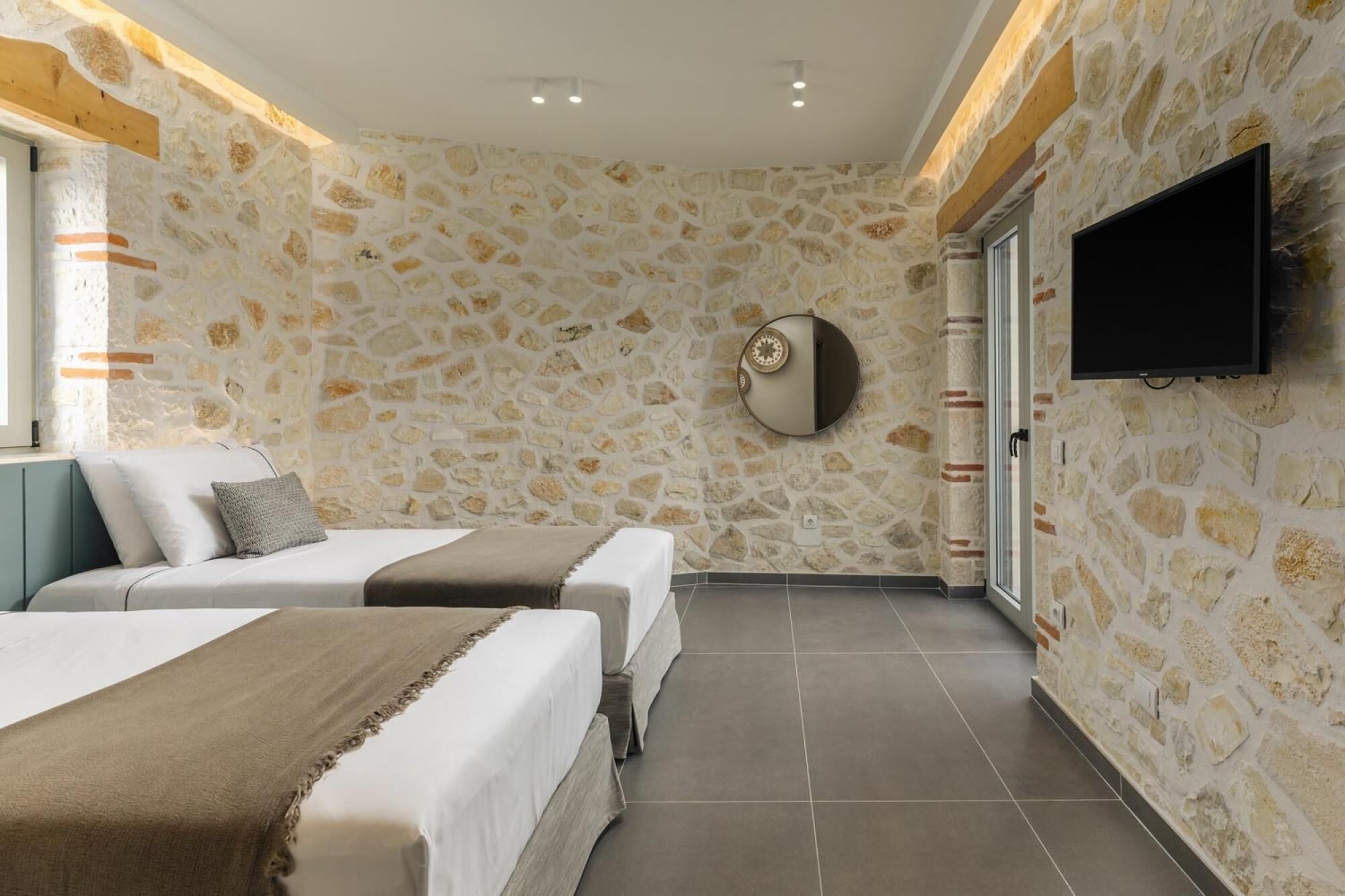 A hotel room with stone walls, a flat-screen TV, two beds, and a large mirror.