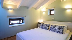 Un dormitorio con cama, mesitas de noche, ventana y luces fijadas a la pared.