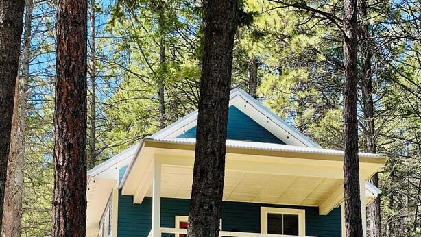 Une cabane à deux étages avec un balcon, entourée d’arbres.