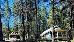 Deux cabanes dans une forêt, l’une avec un porche et l’autre avec une terrasse couverte.