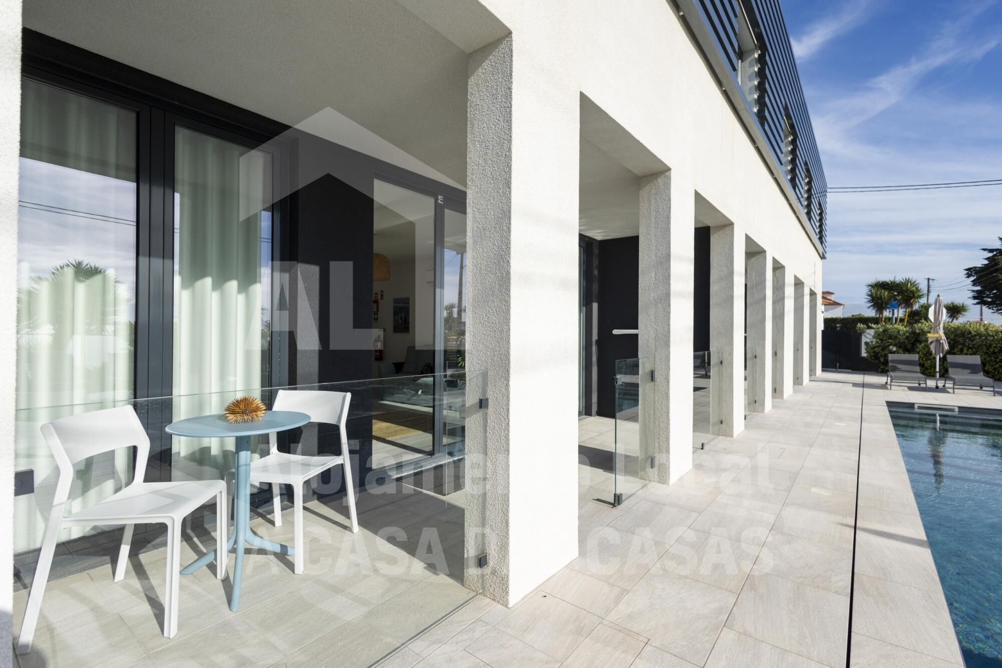 A modern outdoor area with a pool, white chairs, and a glass table.