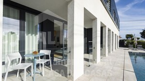 Un espacio exterior moderno con piscina, sillas blancas y una mesa de vidrio.