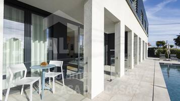 A modern outdoor area with a pool, white chairs, and a glass table.