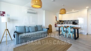 Una sala de estar moderna con un sofá, una mesa de comedor con sillas y una zona de cocina con armarios blancos y un salpicadero decorado.