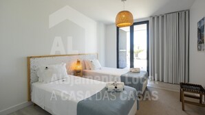 Habitación de hotel moderna con una cama grande, una cama más pequeña, un área de descanso y un amplio ventanal con cortinas.