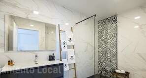 Un baño moderno con tocador de mármol, un espejo grande, ducha con puerta de vidrio con diseño y un taburete pequeño de madera.