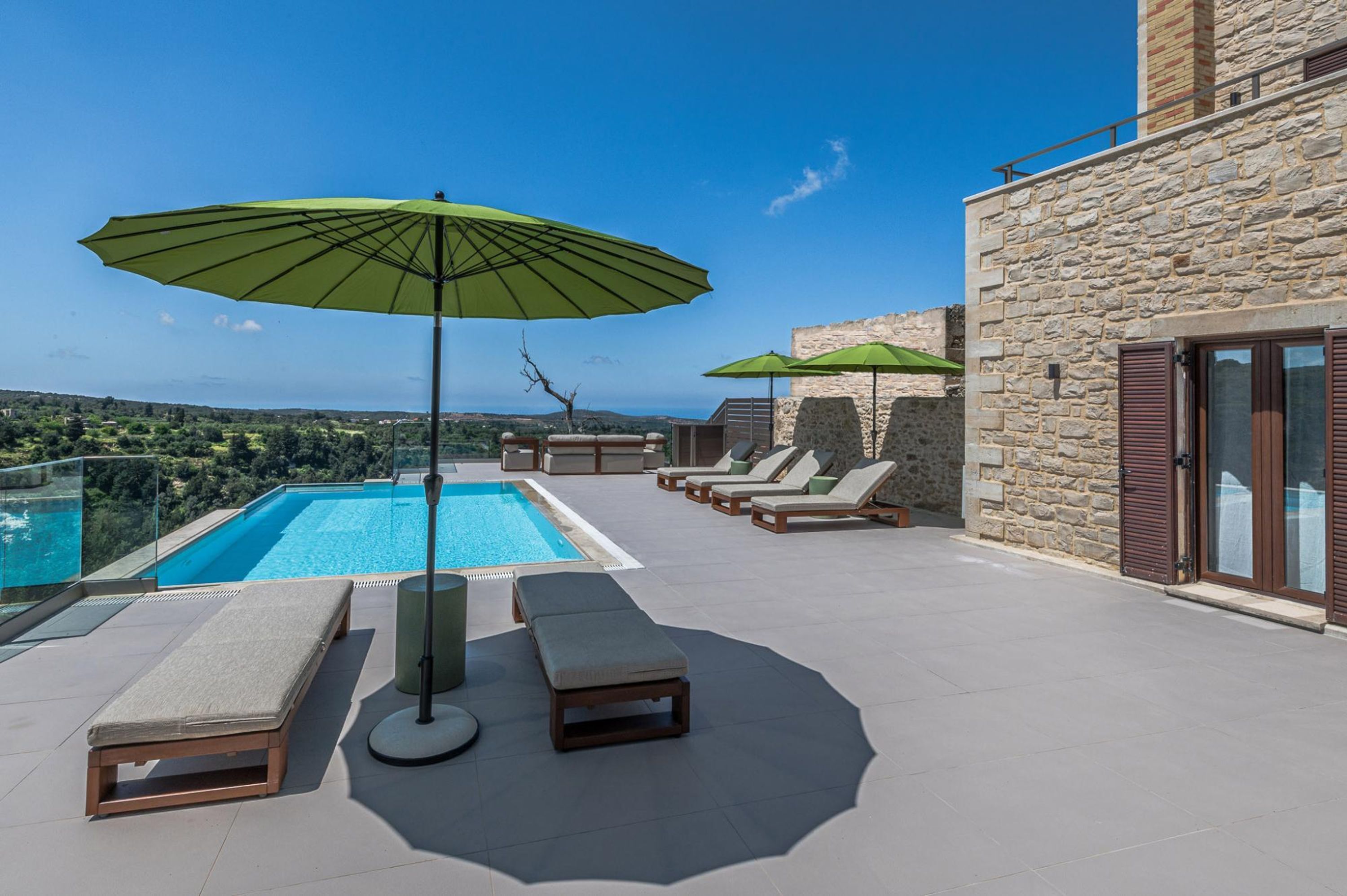A rooftop pool area with lounge chairs and umbrellas, overlooking a scenic landscape.