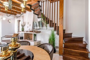 A modern living room with a wooden staircase, a dining area with a round table, and a TV mounted on the wall.