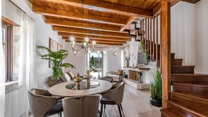 A spacious dining area with a round table and modern chairs, a wooden ceiling, and a staircase leading to an upper level. - Dim Luxury Villa - With Private Pool (Mylopotamos)