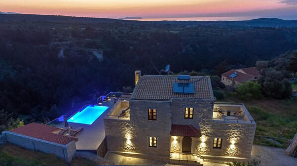 A stone building with a swimming pool, surrounded by a hilly landscape.