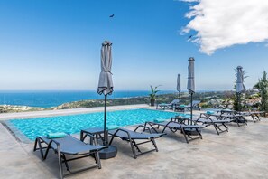 A poolside area with lounge chairs and umbrellas, overlooking a scenic view of the sea and hills. - Villa Eagles - With Private Pool (Rethymno)