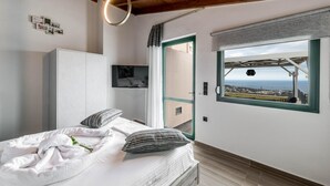 A bedroom with a bed, a wardrobe, a television, and a window with a view of the sea. - Villa Eagles - With Private Pool (Rethymno)