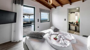 A modern bedroom with a large bed, a TV, a balcony with a view, and a bathroom with a sink and mirror. - Villa Eagles - With Private Pool (Rethymno)