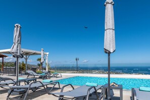 A poolside area with lounge chairs and umbrellas, overlooking a clear blue sky and a distant view of the sea. - Villa Eagles - With Private Pool (Rethymno)