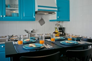 Una cocina con armarios azules, encimera negra y una disposición para el desayuno con platos, panecillos y vasos de zumo de naranja.