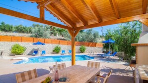 A covered outdoor area with a pool, lounge chairs, and a dining table with chairs. - Blue Villa 1 - With Private Pool (Mylopotamos)