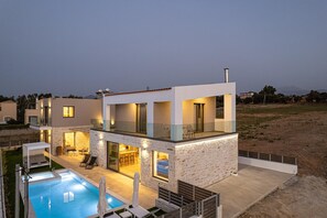 A modern two-story house with a swimming pool, outdoor seating, and a stone facade. - Dodici Luxury Villa - With Heated Pool (Mylopotamos)