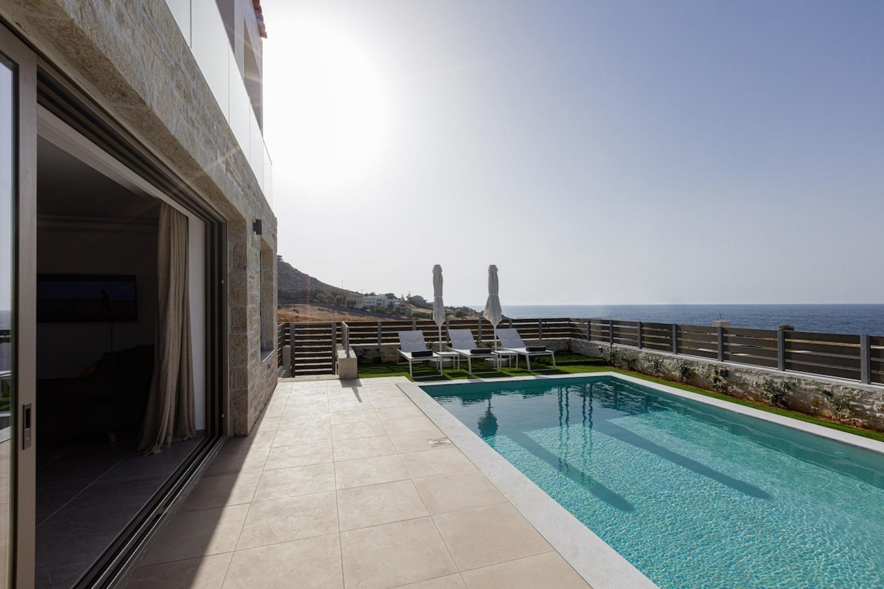 Un espace aménagé au bord de la piscine, offrant une vue dégagée sur la mer, un bâtiment en pierre et quelques chaises longues.