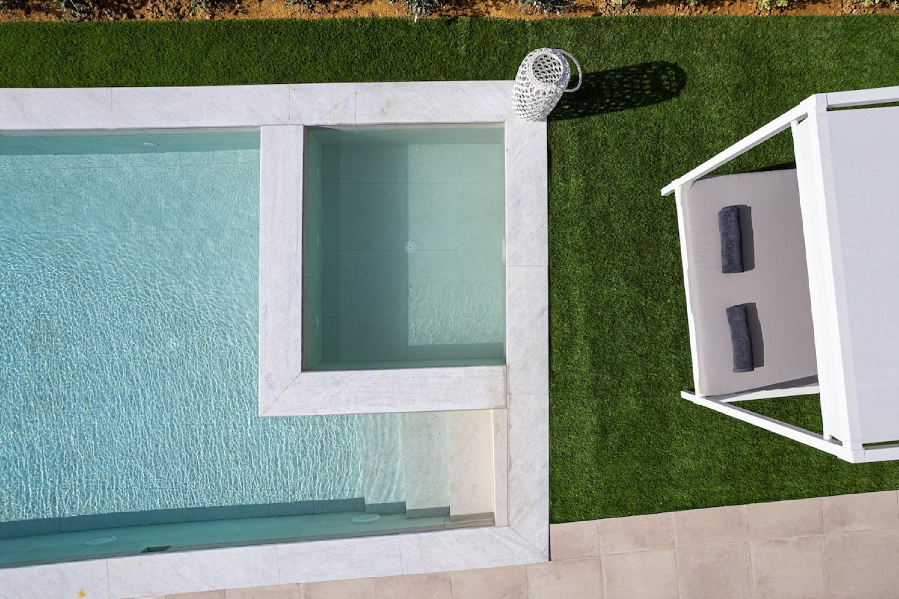 A rectangular swimming pool with a white deck and a white lounge chair on the right.