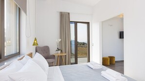 Une chambre d’hôtel moderne avec un grand lit, un petit bureau, une chaise, une vue à travers une porte vitrée et un téléviseur à écran plat fixé au mur.