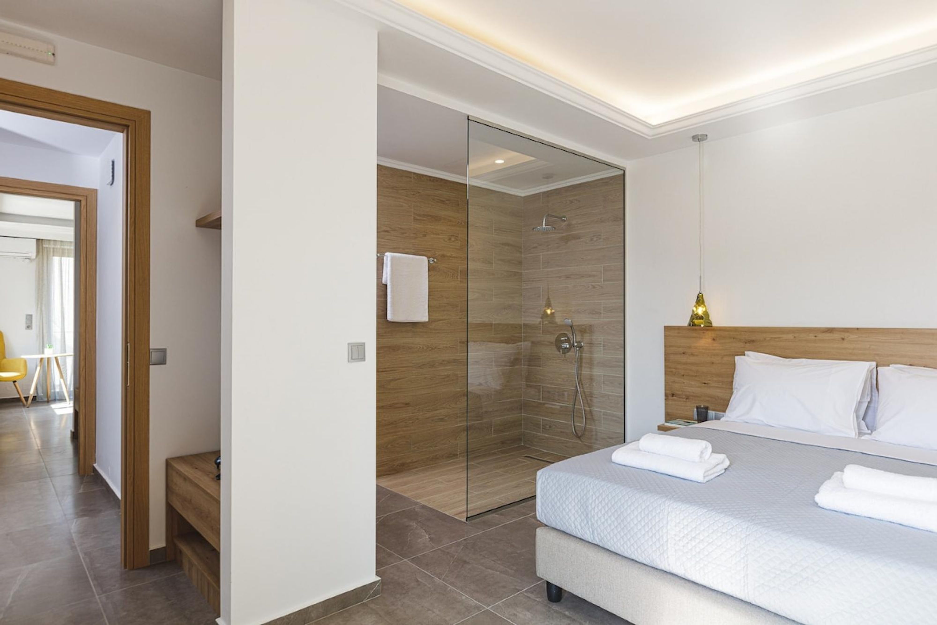 A modern hotel room with a large bed, a glass shower enclosure, and a wooden headboard.