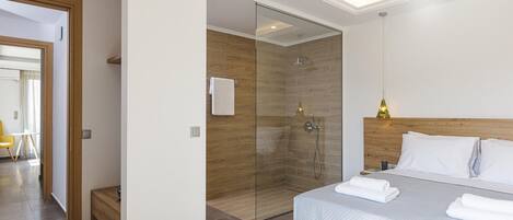 A modern hotel room with a large bed, a glass shower enclosure, and a wooden headboard.