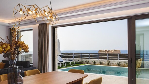 Une chambre d’hôtel moderne dotée d’un coin repas, d’une grande fenêtre offrant une vue sur la mer et d’un espace piscine.