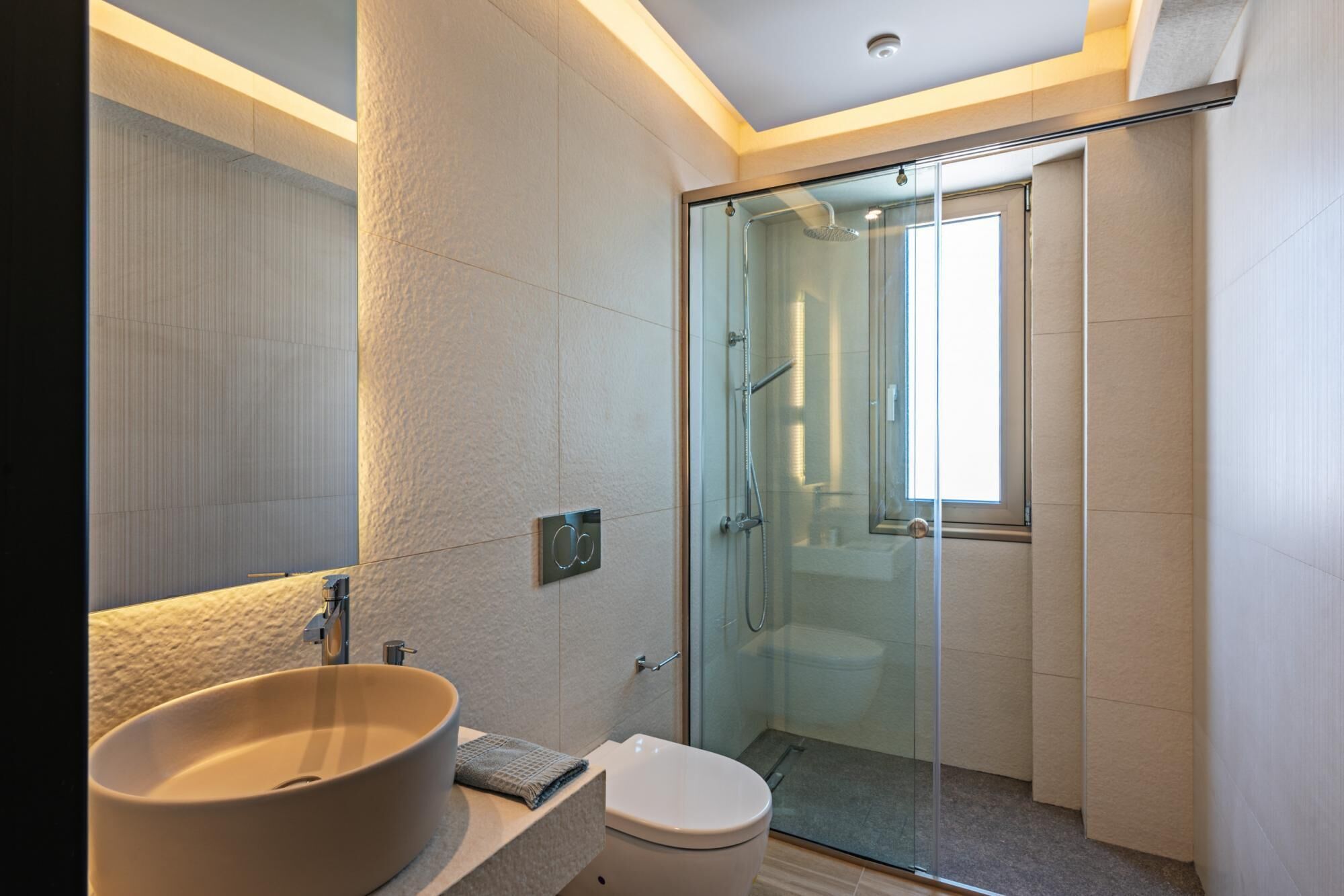 Een moderne badkamer met een groot ovaal wastafel, een douchecabine van glas en een toilet.