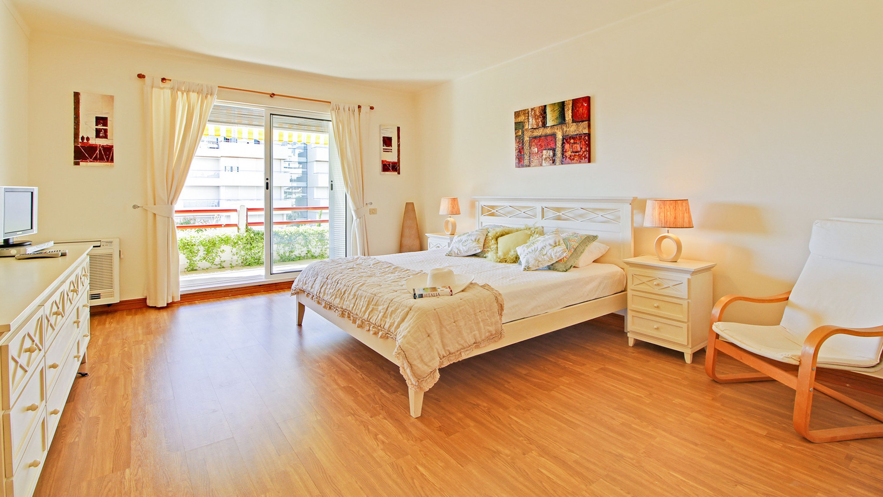 A bedroom with a bed, bedside tables, a chair, a desk with a computer, and a window with curtains.