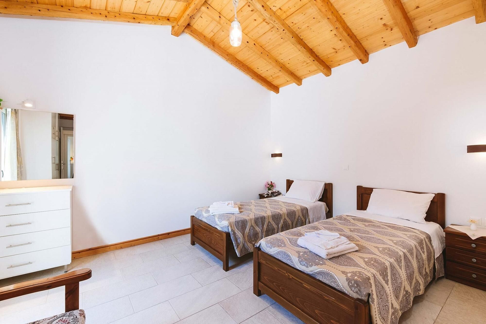 Een slaapkamer met twee houten bedden, een witte kapstok en een houten plafond.