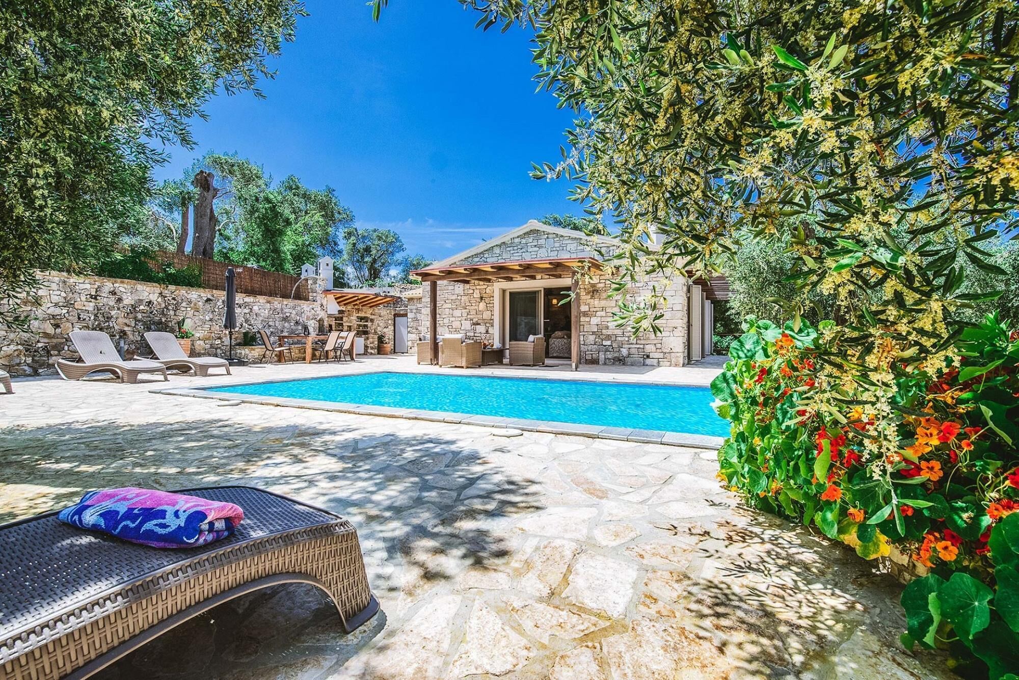A pool area with lounge chairs and a stone building.