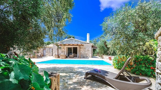 A stone house with a pool, surrounded by lush greenery and a clear blue sky. - Aristea - 2 BR Villa Surrounded by Olive Groves (Paxos)