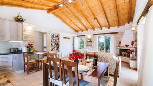 A cozy kitchen with wooden beams, a dining area with a table set for two, and a fireplace with flowers. - Aristea - 2 BR Villa Surrounded by Olive Groves (Paxos)