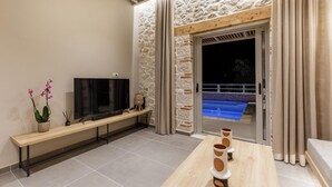 A modern living room with a stone wall, a flat-screen TV, a wooden bench, and a dining table with decorative items. - Armonia II Villa in Paxi (Paxos)