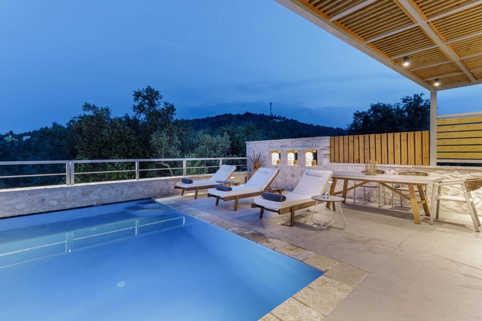Un espace piscine aménagé sur le toit, avec des chaises longues et une table, entouré de murs en pierre et d’une pergola en bois.