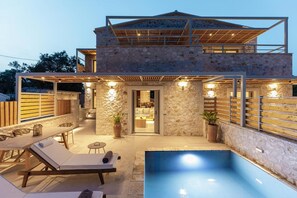 A modern stone house with a pool, outdoor seating, and a covered patio area.