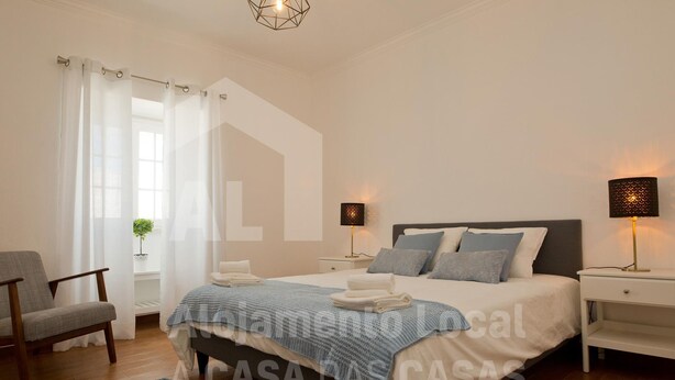 A bedroom with a bed, two bedside tables, a chair, and a window with curtains. - White House by Acasadascasas (Mafra)