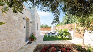 A stone building with a garden area featuring red and white flowers, a wooden fence, and outdoor furniture. - Villa Vera - With Private Pool Jacuzzi (Rethymno)