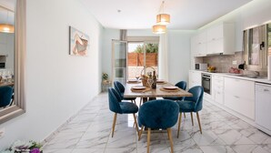 A modern kitchen with white cabinets, a dining area with blue chairs, and a large window. - Villa Vera - With Private Pool Jacuzzi (Rethymno)
